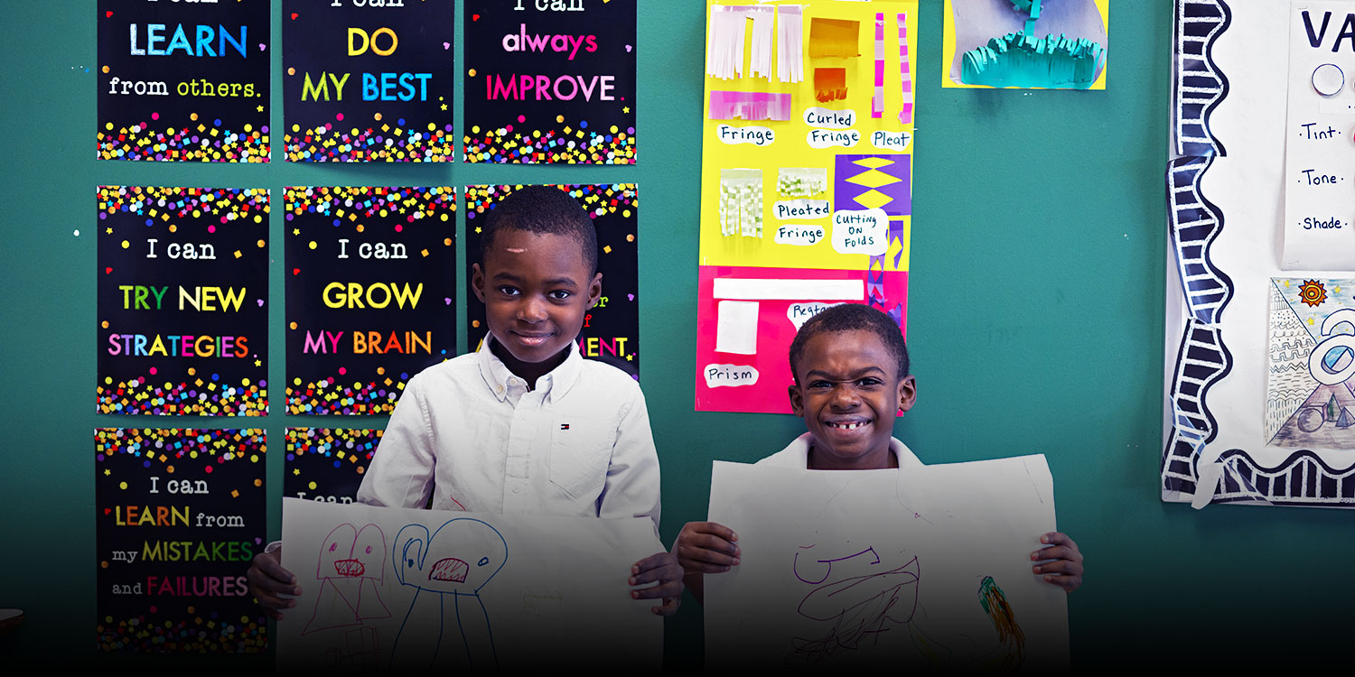 Two smiling students in the classroom with a drawing in their hands